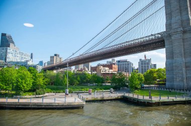 İnsanlar Brooklyn Köprüsü 'nün altında güneşli bir günün tadını çıkarıyor. İnsanlar Manhattan 'daki Brooklyn Köprüsü' nün kıyısında toplanıp New York 'ta güneşli ve sıcak bir günün tadını çıkarıyorlar..