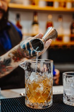 Denver, ABD, 14 Ağustos 2024: Barmen bir barda kokteyli ustalıkla karıştırıyor. Yetenekli bir barmen kristal karıştırma bardağına içki dökerken canlı bir barda kokteyl hazırlar..
