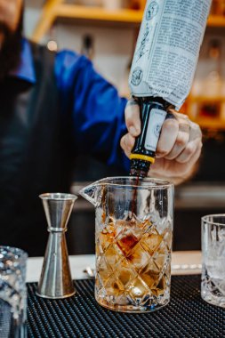 Denver, ABD, 14 Ağustos 2024: Barmen bir barda kokteyl hazırlıyor. Uzman barmen, barda canlı bir akşam kokteyli hazırlarken bardağa malzemeler doldurur..