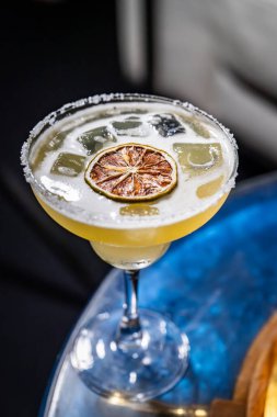 Kurutulmuş kireç garnitürle servis edilen ferahlatıcı kokteyl. Buzlu renkli bir kokteyl ve üstünde kurutulmuş limon dilimi, şık bir masa ayarında, her toplanma için mükemmel..