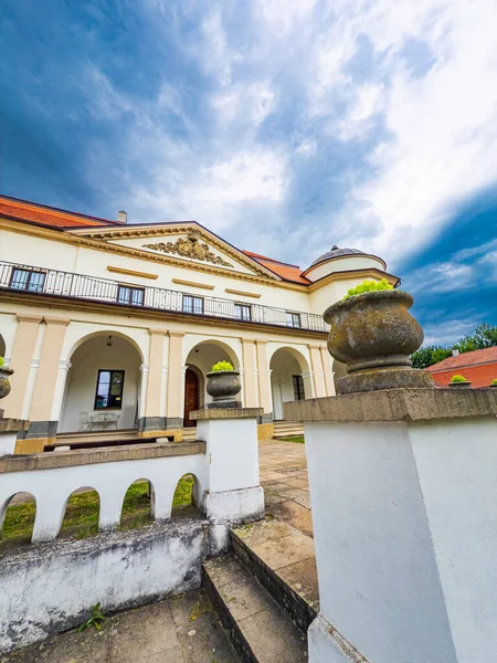 İlkbaharda dramatik bir gökyüzü altında tarihi bir bina. İlkbaharda bulutlu mavi gökyüzüne karşı dizilmiş kavisli kolonlara ve canlı yeşilliklere sahip zarif tarihi yapı..