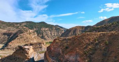 ABD 'nin Utah eyaletindeki Price Kanyonu' nun dağlık arazisinden yükseliyor. Dalgalı yolları ve kayalık bölgeden geçen arabaları izle..