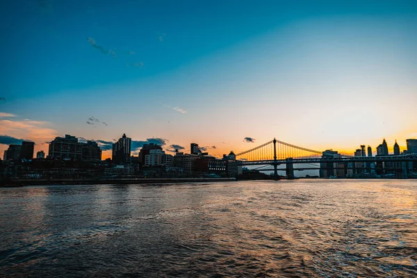 Gün batımında nehir üzerinde köprü. Brooklyn Köprüsü ve New York Şehri ufuk çizgisi.