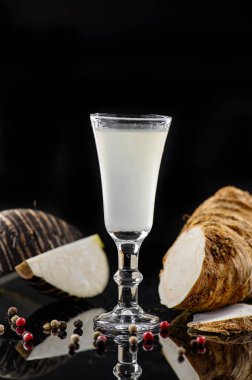 Siyah arka planda fındıklı beyaz hindistan cevizi likörü. Beyaz hindistan cevizi likörlü shot bardağı siyah arka planda çatlak bir hindistan cevizinin yanında duruyor..