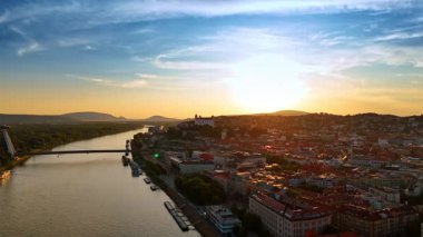 Günbatımında Bratislava ufuk çizgisine bakan Tuna Nehri. Tuna Nehri, ufukta Bratislava şehrinin ufuk çizgisi olan ılık günbatımı ışığını yansıtır..