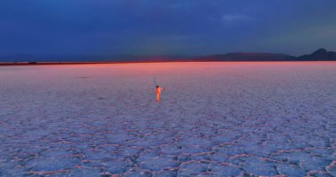 Beyaz takım elbiseli adam gün batımında engin tuzlu arazide duruyor. Drone o kişiye yaklaşıyor ve kaçıyor. Bonneville Tuz Düzlükleri, Kuzeybatı Utah, ABD.