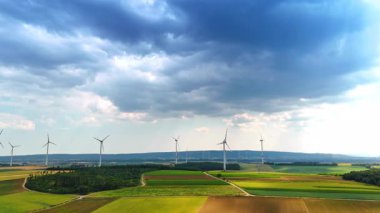 Rüzgar çiftlikleri geniş kırsal alanda sürdürülebilir enerji üretir. Gri bulutlar gökyüzünü kaplıyor.
