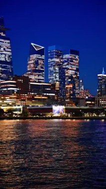 New York 'un gökdelenleri pencereleri açık muhteşem gökdelenler. Geceleri nehir manzaralı şehir manzarası. Dikey video.