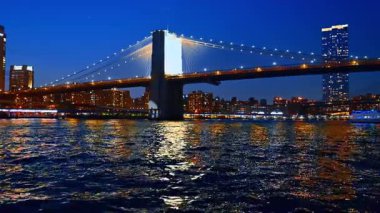 Gece Brooklyn Köprüsü 'nün aydınlatılması. Doğu Nehri 'nin çalkantılı nehir manzarasından alçak açı..