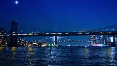 Brooklyn Köprüsü ve Manhattan Köprüsü gece aydınlatmayı açtı. Nehir manzarasından şehre alçak açılı görüş.