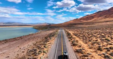 Su manzarası boyunca otoban boyunca giden bir arabayı takip ediyorum. Güzel dağ sıraları ve mavi gökyüzünde kabarık bulutlar.