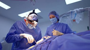 Cerrahi mikroskobu olan beyin cerrahı bir hasta. Koruyucu maskeli doktor hassas beyin ameliyatı için mikroskop kullanıyor. Hastane ortamında modern nörocerrahi teknolojileri.