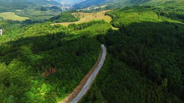 Yeşil tepeler arasında yolu olan dağ vadisi ormanlık tepelerden geçen dar bir yolun havadan görünüşü. Vadi tarlalara ve uzak dağlara açılıyor..