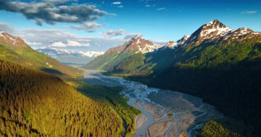 Çam ağaçlarıyla kaplı muhteşem dağların manzarası ve tepesinde biraz kar var. Dallanan sığ nehir vadiyi kayalıklardan geçer. Hava görüntüsü. Alaska, ABD.