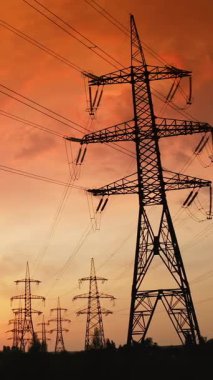 Gün batımında yüksek voltaj santrali. Metal direkleri ve elektrik kabloları olan elektrik iletim istasyonu.