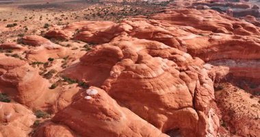 Sıcak çöldeki pürüzsüz kırmızı kanyonların üzerinden uçmak. Arka planda yeşil küçük çalılarla kaplı bir manzara. Arches Ulusal Parkı, Utah, ABD.