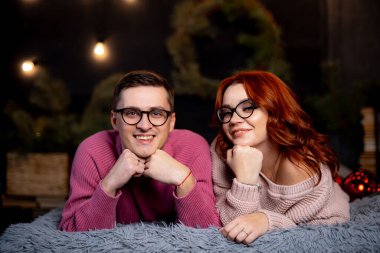 Çiftler kış mevsiminde evlerinde rahat bir akşam geçirirler. Genç bir çift yumuşak bir halının üzerinde rahatlar, gülümser ve birlikte poz verirler, sıcak, rahat bir oturma odasında, şenlikli bir dekorla..