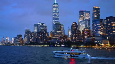 Gece Hudson Nehri 'nde lüks bir yat gezintisi. Beyaz lüks bir yat Hudson Nehri 'ni geçiyor. Arka planda Manhattan' ın aydınlık silüeti var..
