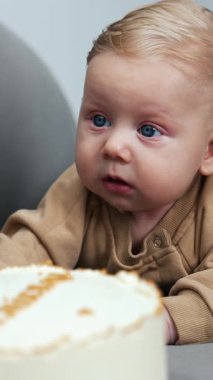 Mavi gözlü erkek bebek bir pastanın önünde yatıyor. Dört aylık bebek karnının üstünde yatıyor. Kapatın. Dikey video