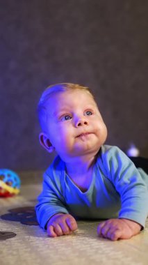 Beyaz saçlı küçük bebek göbeğinde yatıyor. Barışçıl erkek bebek ilgiyle yukarı bakıyor. Dikey video