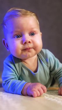 Tombul yanaklı sevimli bebek yerde yatıyor. Sakin bir çocuk ilgiyle ona bakıyor. Arkaplan bulanık. Dikey video