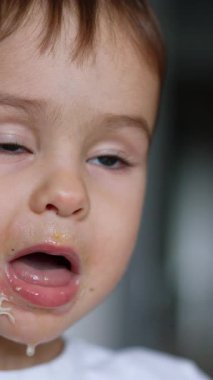 Tatlı beyaz çocuk çorbanın tadını çıkarıyor. Sevimli çocuk kaşığı dolduruyor ve yemeğinin tadına bakıyor. Kapatın. Arkaplan bulanık. Dikey video