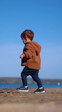 Küçük çocuk bir taş seçiyor ve suya giriyor. Enerjik çocuk taşı nehre atıyor. Düşük açı. Dikey video