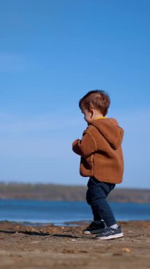 Nehre doğru yürüyen tatlı çocuk. Şirin küçük çocuk taşı suya attı ve uzaklaştı. Dikey video