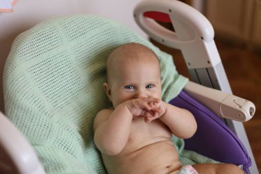 Mavi gözlü beyaz bebek yeşil bir battaniyenin üzerinde bir sandalyede yatıyor ve gülümsüyor.