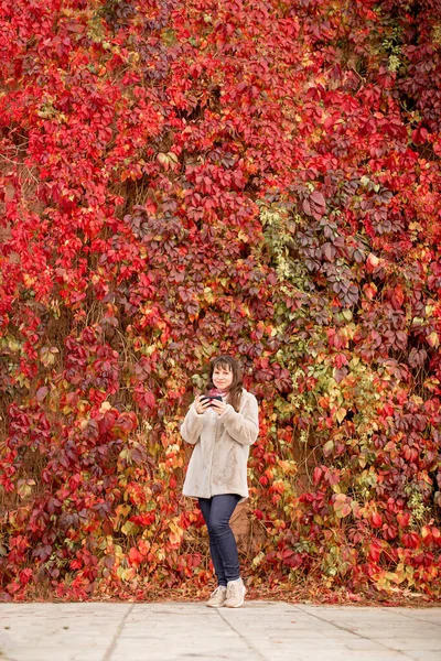 Dziewczyna Beżowym Płaszczu Stoi Obok Czerwonej Ściany Winogron Jesienią — Zdjęcie stockowe