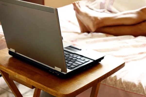 Ahşap bir masa ve bir kişinin bacakları üzerinde Dizüstü bilgisayar — Stok fotoğraf