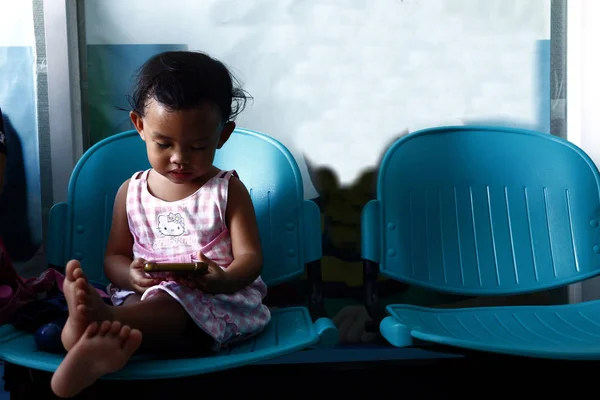 Young Asian girl plays a video game on a smartphone while at a waiting area. — Stock Photo, Image