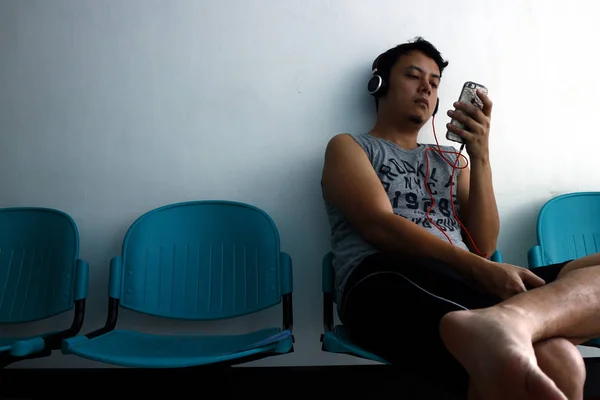 Ein erwachsener philippinischer Mann benutzt ein Smartphone, während er auf einer Bank sitzt — Stockfoto