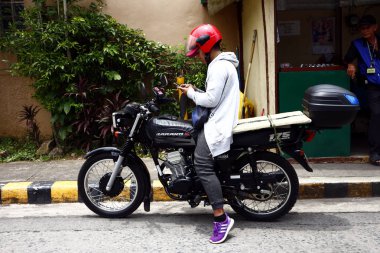 Bir motosiklet sürücüsü, akıllı telefonunu kontrol etmek için bir kaldırımda durur.