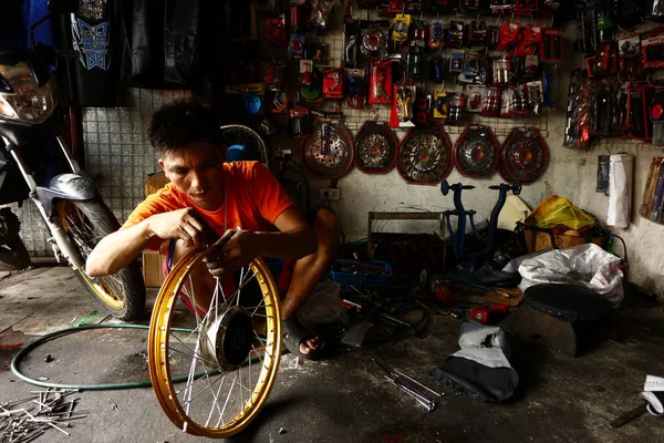 A worker at a motorcycle repair shop fix the spokes of a motorbike���s wheel. — Stock Photo, Image