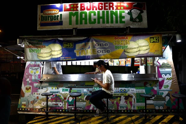 Ein Kunde an einem Hamburger-Stand benutzt sein Smartphone, während er auf sein Essen wartet. — Stockfoto