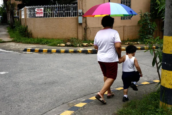 Una mujer sostiene la mano de un niño mientras camina en una acera de una calle . — Foto de Stock