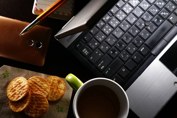 Bärbar dator, kopp kaffe, Ballpen, anteckningsbok, crackers och en smartphone — Stockfoto