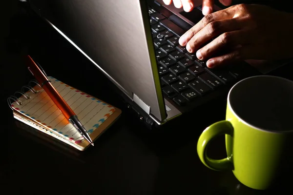 Mão em um computador portátil, xícara de café, esferográfica e um caderno — Fotografia de Stock