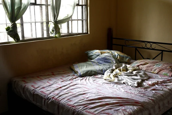 Messy bed beside bedroom window