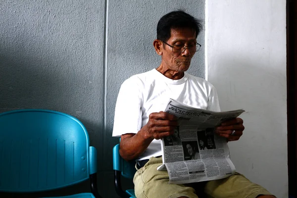 Senior Filipino man read newspaper while at waiting area. — Stock Photo, Image