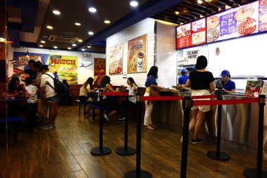 Pizza restoranındaki müşteriler kasiyerden sipariş verip yemeklerini yiyorlar..