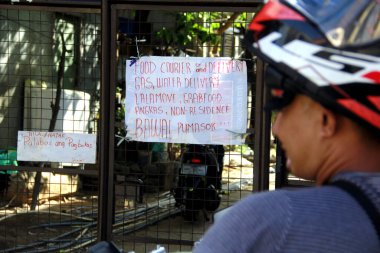 Antipolo Şehri, Filipinler - 2 Haziran 2020: Bir motosiklet teslimatçısı, Covid 19 virüs salgını sırasında kapalı bir toplulukta yabancıların imzasına izin verilmediğine bakıyor.