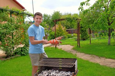 Daha önce gülümseyen genç çocuk elinde ızgara şiş üzerinde ham Barbekü