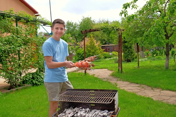 Daha önce gülümseyen genç çocuk elinde ızgara şiş üzerinde ham Barbekü