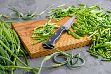 Sağlıklı doğal vegan gıda. Gri beton zemin üzerine bir ışık ahşap kesme tahtası üzerinde birçok dilimler halinde okları genç taze sarımsak kıyılmış