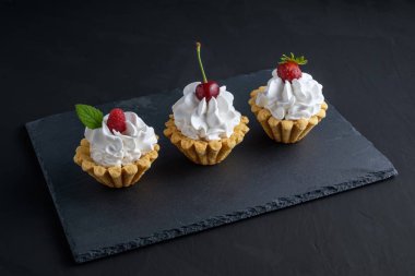 Protein krem ve siyah arka plan üzerinde koyu taş plaka üzerinde yaz meyveleri ile üç kek