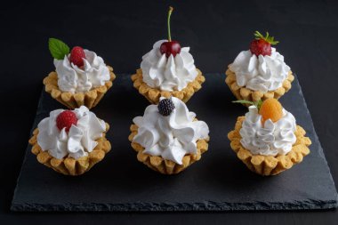 Protein krem ve siyah arka plan üzerinde koyu taş plaka üzerinde yaz meyveleri ile altı kek. Yakın çekim görünümü