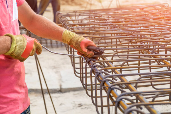 Hands of worker in protective gloves knit metal rods with wire for concrete reinforcement