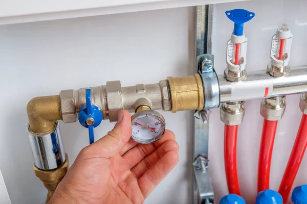 The plumber hand connects the thermometer to the supply pipe of collector for the warm floor. Closeup view